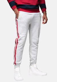 Helle graue Baumwoll-Sweatpants mit roten Seitenstreifen, gerippten Knöchelbündchen und zwei Seitentaschen. Tragen Sie dazu weiße High-Top-Sneaker.