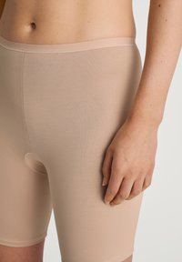 Beige seamless boyshorts made of soft, stretchy fabric, featuring a snug fit and a circular cut-out detail. Smooth texture and waistband.