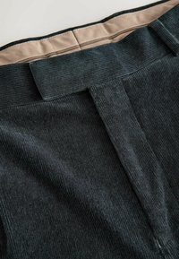 Black corduroy pants featuring a smooth waistband, vertical ribbed texture, and clean finish on the back seam. Interior is beige.