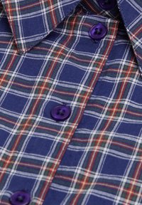 Geruit shirt met een marineblauwe basis, met een witte, groene en rode ruitpatroon en paarse knopen. Zachte stof met een kraagontwerp.