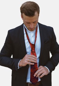 Corbata de seda de rayas paisley rojas, combinada con un traje oscuro. La corbata tiene un diseño delgado con una textura suave y un acabado brillante.