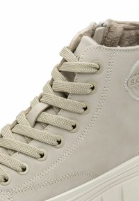 Baskets hautes beiges avec une tige en synthétique texturé, des lacets assortis et un logo sur le côté. Elles présentent un col rembourré et une semelle épaisse.