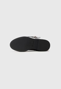 Melna zole mūsu apavu ar teksturētiem saķeres laukumiem un zīmola nosaukumu "Steve Madden" iepresēts tuvāk arkam.