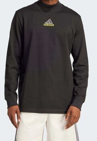 Black long-sleeve sweatshirt made of cotton blend, featuring a high neck and a yellow adidas logo centered on the chest. Smooth texture.