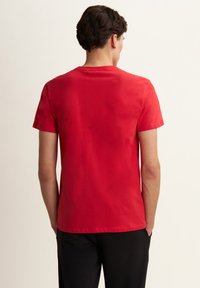 T-shirt in cotone rosso con maniche corte e scollatura rotonda, mostrata da dietro. Tessuto liscio, design aderente e senza loghi visibili.