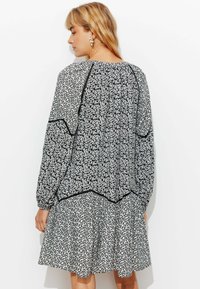 Robe florale noire et blanche à manches longues, avec un design plissé et une bordure noire contrastante le long du col et de l'ourlet.