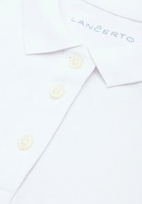 Biała koszulka polo z teksturowanym splotem bawełnianym, z miękkim kołnierzykiem i trzema kremowymi guzikami przy zapięciu. Wewnątrz kołnierzyka widoczna metka marki.