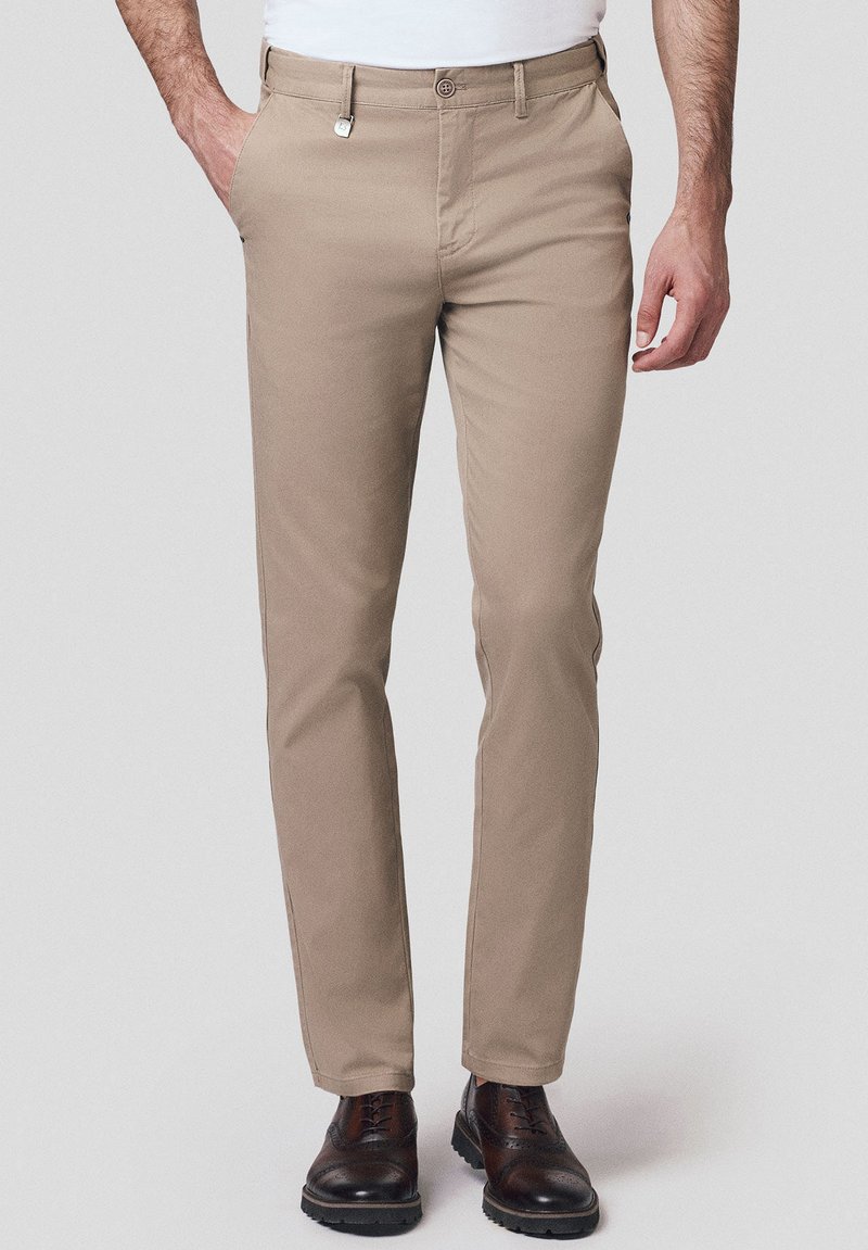 Beżowe chinosy o dopasowanym kroju, wykonane z gładkiego materiału. Posiadają kieszenie z przodu, szlufki na pasek oraz mały srebrny detal w postaci guzika.
