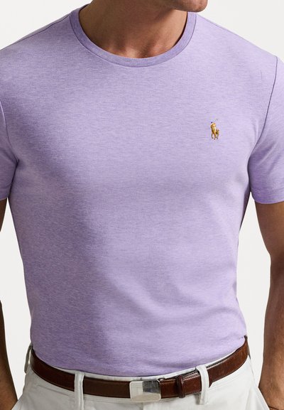 Μωβ μπλουζάκι crew-neck φτιαγμένο από βαμβακερό ύφασμα, με ένα μικρό κεντημένο λογότυπο στο στήθος και λείο, ελαφρώς υφασμένο επιφάνεια.