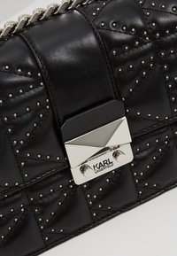 Borsa a tracolla nera in pelle trapuntata con borchie argentate, un gancio metallico con il logo di Karl Lagerfeld e una tracolla a catena.