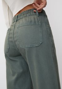 Pantalon coupe décontractée de couleur vert olive avec tissu texturé, taille élastique et deux poches plaquées à l'arrière.