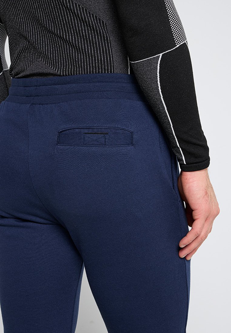 Dunkelblaue Sportpants mit einer Gesäßtasche und elastischem Bund. Aus einem glatten Stoff gefertigt, taillierte Passform. Sichtbares strukturiertes schwarzes Langarmoberteil.