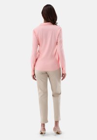 Light pink long-sleeve polo shirt with a collar, paired with beige fitted pants. The shirt features a smooth texture and subtle design details.