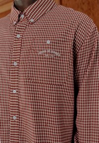 Κόκκινο και λευκό πουκάμισο με κουμπιά και καρό σχέδιο, με τσέπη στο στήθος και κεντημένο κείμενο "House of Sunny" στην τσέπη.