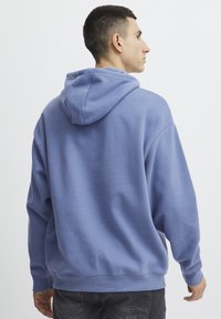 Felpa leggera azzurra realizzata in materiale morbido, con tasca a marsupio, cappuccio regolabile con cordino e polsini e orlo a costine.
