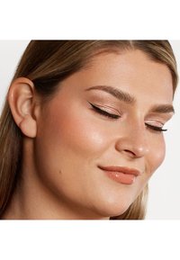 Primo piano di un volto con una pelle liscia. Le caratteristiche includono capelli castano chiaro, sopracciglia definite, ombretto luccicante e rossetto nude lucido.