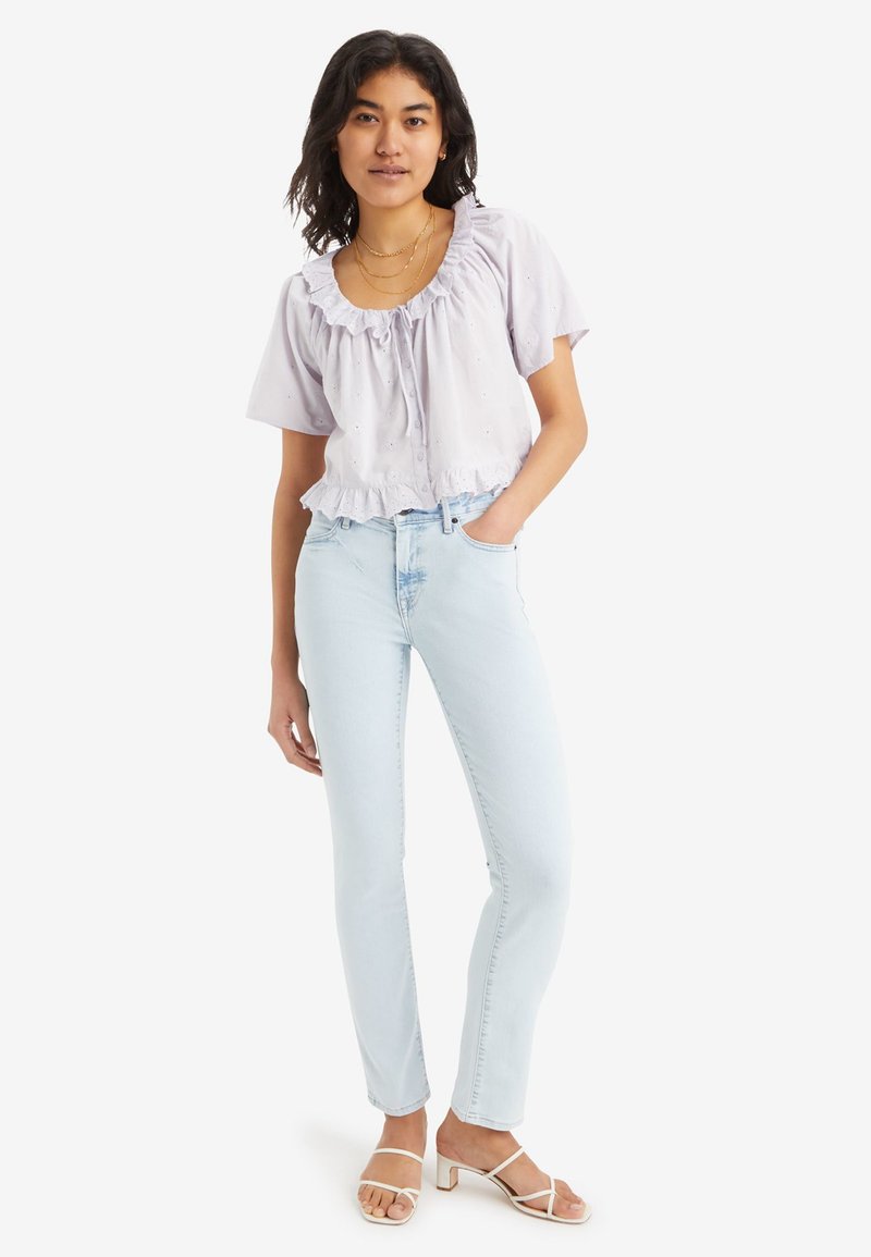 Helles lila kurzes Oberteil mit Rüschenausschnitt und bestickten Details; kombiniert mit hellblauen Skinny Jeans und weißen, gestrickten Blockabsatzsandalen.