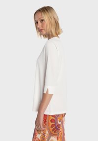 Top blanco, ligero, de manga tres cuartos con aberturas laterales; combinado con una falda vibrante y estampada que presenta tonos rojos, naranjas y morados.