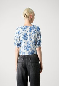Bluse med blomsterprint i lyseblå og hvit, med puffede ermer og en tettsittende silhuett, kombinert med høyt liv mørke jeans.