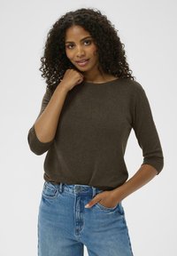 Brązowy, długi sweter z okrągłym dekoltem i fakturowaną tkaniną, w połączeniu z jasnoniebieskimi dżinsami z wysokim stanem. Luźny krój.