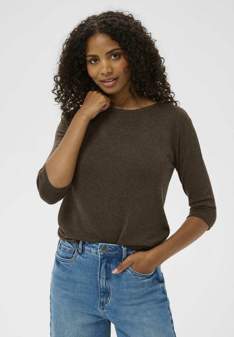 Brązowy, długi sweter z okrągłym dekoltem i fakturowaną tkaniną, w połączeniu z jasnoniebieskimi dżinsami z wysokim stanem. Luźny krój.