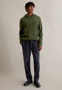 Πράσινο φούτερ με κουκούλα και υφή, συνδυασμένο με σκούρα ναυτικά παντελόνια από κορντούρα με κάθετες ρίγες. Μαύρες μπότες έως τον αστράγαλο ολοκληρώνουν την εμφάνιση.