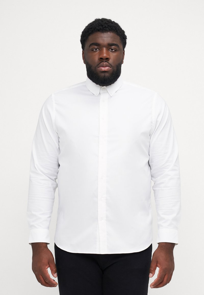 Camicia bianca a maniche lunghe con colletto, caratterizzata da una texture liscia e una vestibilità affusolata, indossata con pantaloni scuri.