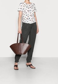 Sac à main marron à motif crocodile avec deux poignées ; assorti à un haut blanc à imprimé papillon et à un pantalon ample gris foncé.