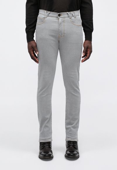 Sivi slim-fit jeans z gladko teksturo, ki vsebujejo vidne šive, pet žepov in zapenjanje z gumbi, oblečeni z črnimi čevlji.