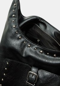 Crna umjetna kožna hobo torba s srebrnim zakovicama duž ruba, unutrašnjim džepom na patentni zatvarač i remenom s metalnom kopčom.
