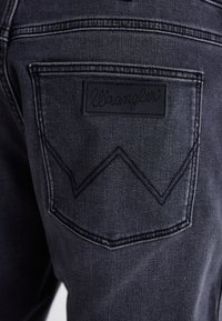 Mustat farkut sisältävät ommellun takataskun, jossa on suorakulmainen nahkaleima, jossa lukee "Wrangler", ja zic-zac kuvio taskun yläpuolella.