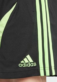 Černé sportovní šortky se zelenými akcenty, s texturovaným panelem a třemi svislými pruhy. Logo na lemu v odpovídající zelené barvě.