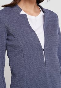 Námořnická pruhovaná bunda se zipem vpředu a designem s vysokým límcem. Měkká, strukturovaná látka s dlouhými rukávy a fitted střihem.