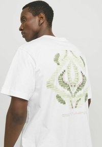 Weißes T-Shirt aus Baumwolle mit einem großen grünen und pinken abstrakten Grafikdesign auf dem Rücken, mit kurzen Ärmeln und einer lockeren Passform.