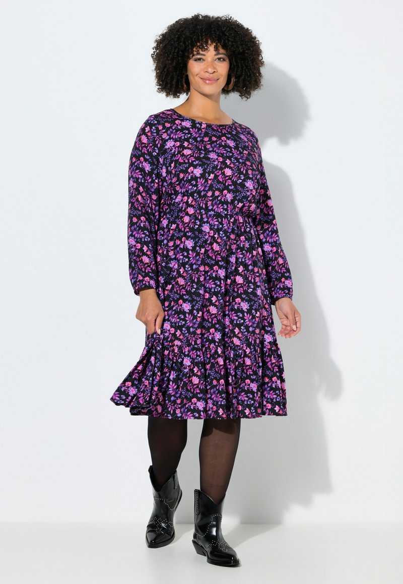 Sukienka w kwiaty na granatowym tle z różowymi i fioletowymi kwiatami, długimi rękawami, falbaną na dole, zestawiona z czarnymi botkami do kostki.