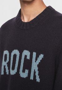 Dunkelblaues Sweatshirt mit geripptem Rundhalsausschnitt, das auf der Brust den Schriftzug "ROCK" in hellblauer Strickschrift trägt. Weicher, strukturierter Stoff.