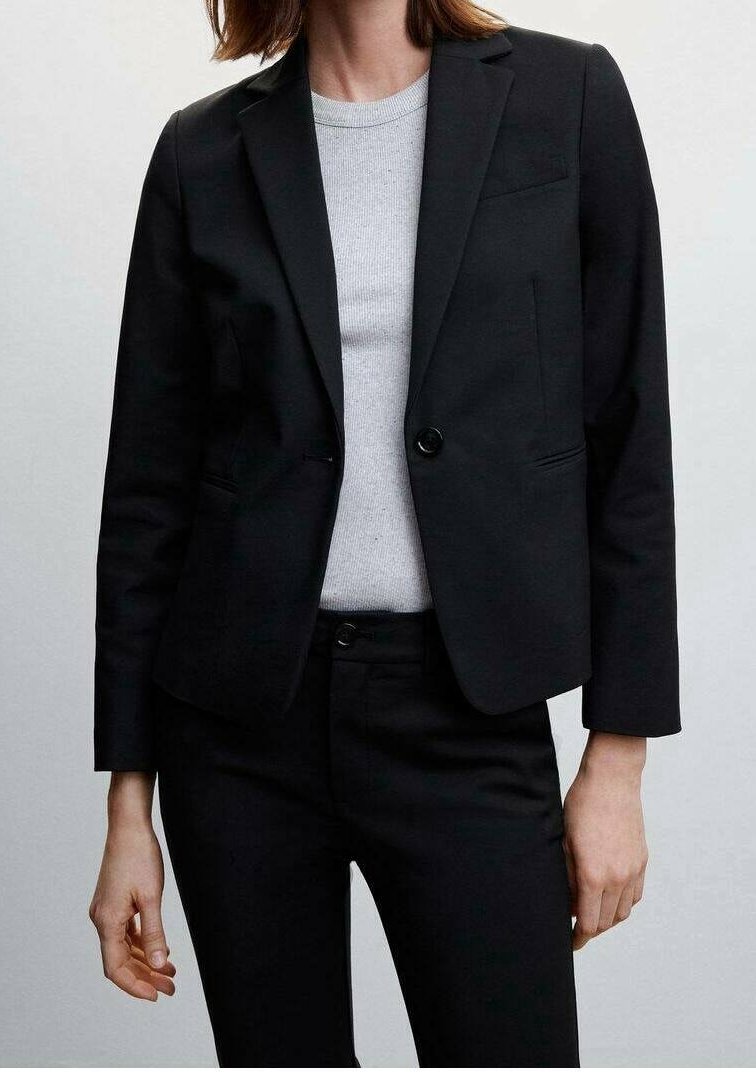 Zwarte op maat gemaakte blazer met een enkele knoopsluiting, notch-revers en twee voorkruiken, gedragen over een lichtgrijze geribde top.