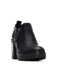 Botas de tobillo negras hechas de cuero sintético suave, con punta redonda, tacón grueso, cremallera lateral y tachuelas decorativas en un lado.