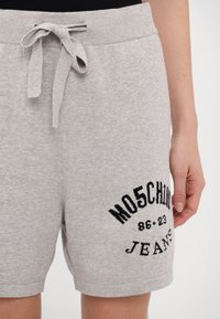 Pilkos medvilnės šortai su ribota juosme, surišami su raišteliu, turi juodą siuvinėtą tekstą ir skaičius šone.