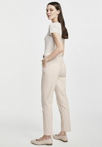 Beżowe dopasowane spodnie o slim fit, z bocznymi kieszeniami i gładkim przodem, zestawione z jasną koszulką i kremowymi butami wsuwanymi.