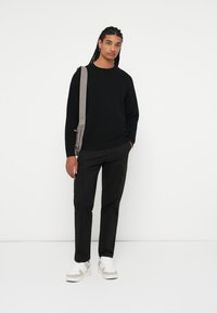 Sort struktureret sweater, sorte cargo-bukser og hvide sneakers med beige detaljer; grå skuldertaske. Enkel, afslappet outfit.