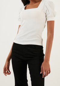 Biała, prążkowana bluzka z krótkim rękawem, z kwadratowym dekoltem i bufkami, w zestawieniu z czarnymi, dopasowanymi spodniami. Teksturowany materiał z delikatnym rozciągnięciem.