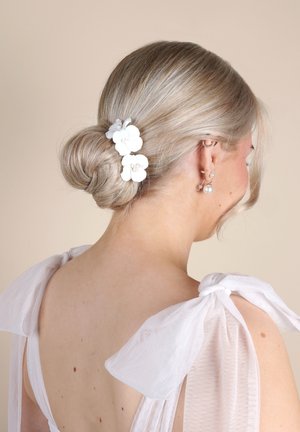 Fermaglio per capelli floreale bianco con accenti di perle, posizionato in uno chignon basso. Lo sfondo è neutro; i capelli sono biondi chiari, acconciati in modo liscio.