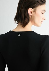 Schwarzes Stricktop mit rundem Ausschnitt, zeigt eine glatte Textur und eine figurbetonte Form. Verfügt über ein kleines Logodetail am rückseitigen Ausschnitt.