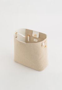 Sac fourre-tout en tissu tissé beige avec des accents en cuir blanc, quincaillerie dorée et une poche intérieure. Il dispose d'une fermeture à pression et d'un design à ouverture supérieure.