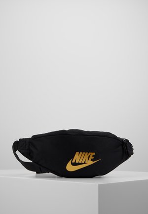 Marsupio nero Nike con logo dorato, posizionato su una superficie bianca con sfondo grigio.