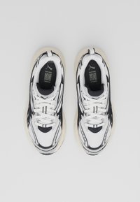 Des sneakers blancs et noirs avec un dessus en maille, plusieurs panneaux texturés, une semelle rembourrée et des accents noirs sur les côtés et la languette.