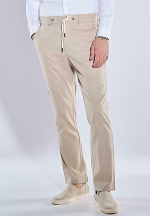 Beige Leinenmischung-Hosen mit Kordelzugverschluss, seitlichen Taschen und einem lockeren Schnitt. Getragen mit hellbeigen Slippern.