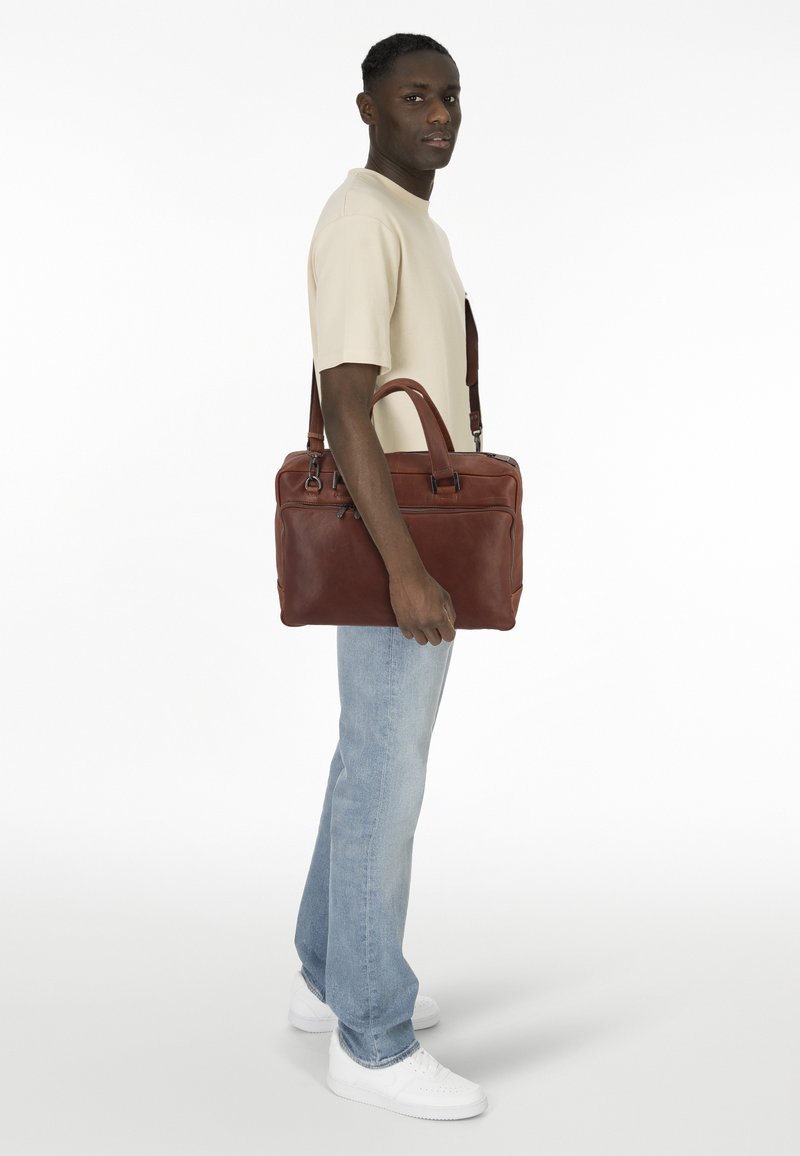 Borsa a tracolla in pelle marrone con doppio manico superiore, tracolla regolabile e chiusura a zip. Caratterizzata da una texture liscia e un design minimalista.