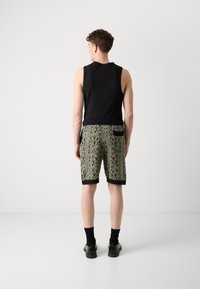 Top negro sin mangas, shorts con un diseño de encaje verde claro, con ribete negro y bolsillo trasero. Llevado con calcetas y zapatos oscuros.